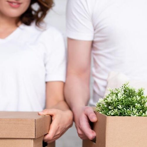 moving day concept - close up of cardboard boxes in young couple hands
